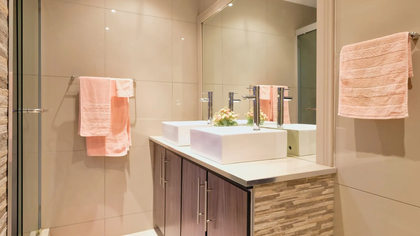 A modern bathroom featuring double sinks, large mirror, and peach towels enhancing elegance.